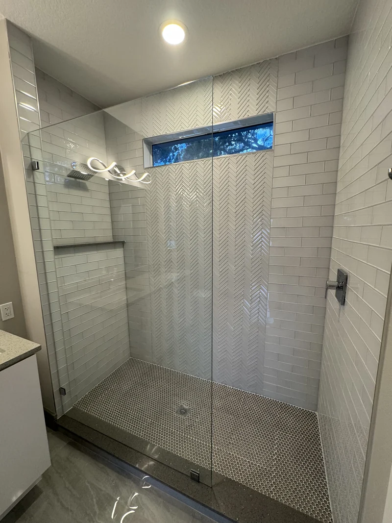Glass shower enclosure with white subway tile and a horizontal window