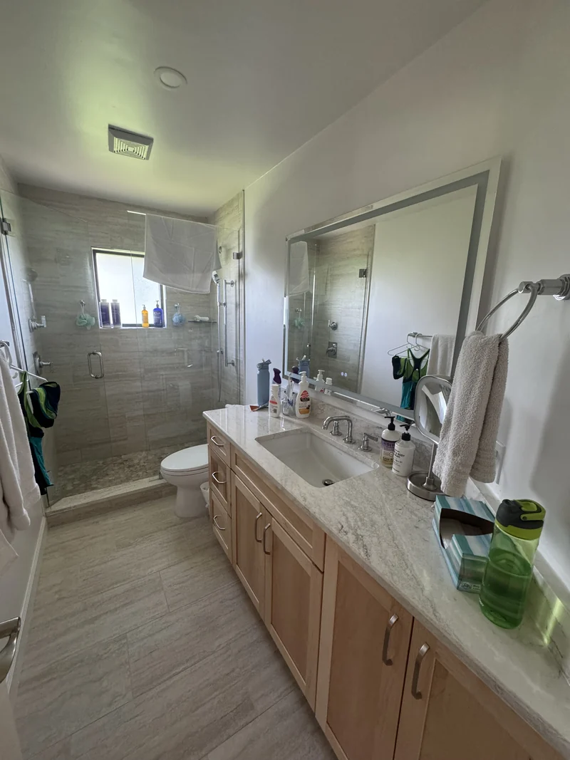 Wood vanity, large mirror and glass shower with warm-toned tile
