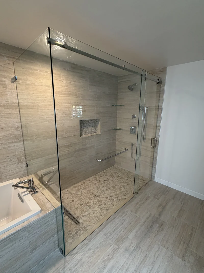 Glass shower enclosure with pale stone-look tile and a recessed niche
