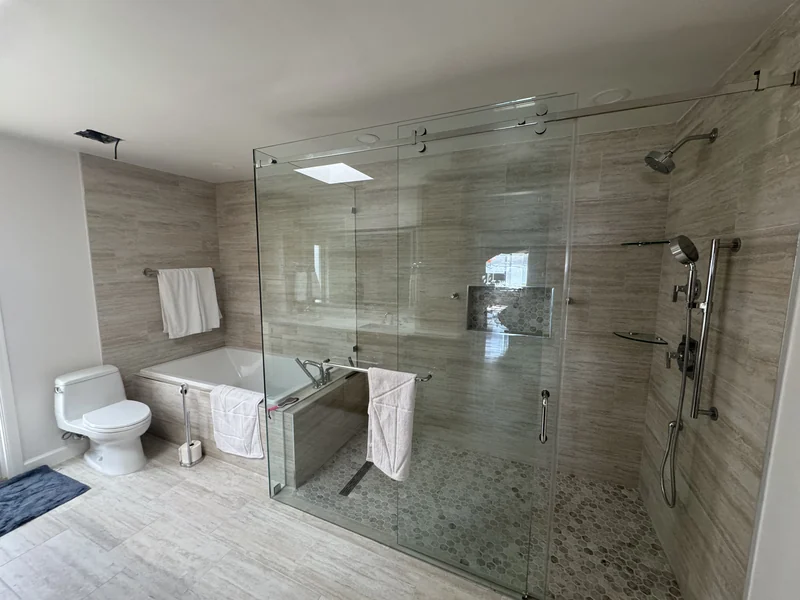 Wide glass shower enclosure with a tiled bench and warm stone-look walls