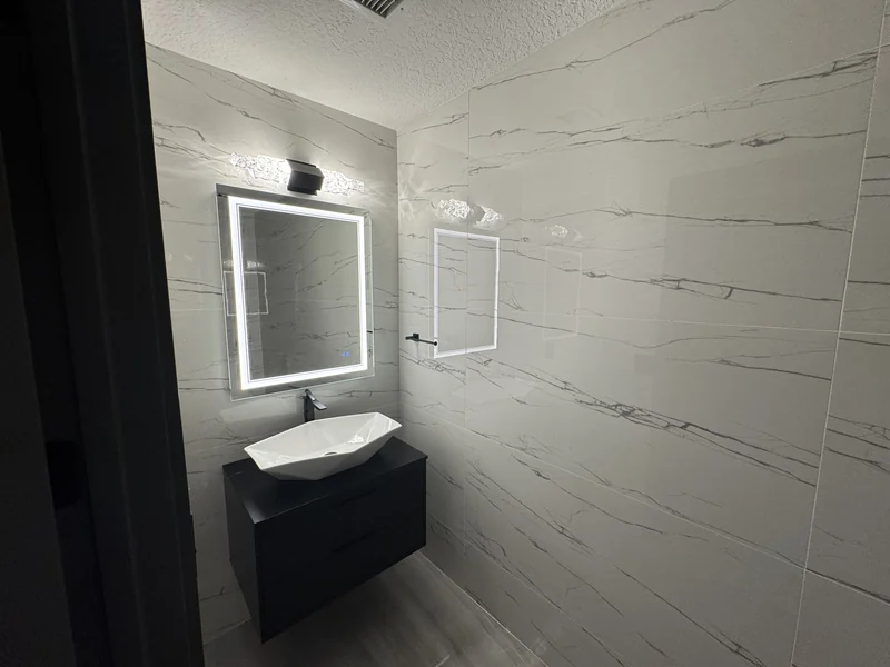 Wall-mounted dark vanity and white basin against veined white wall tile