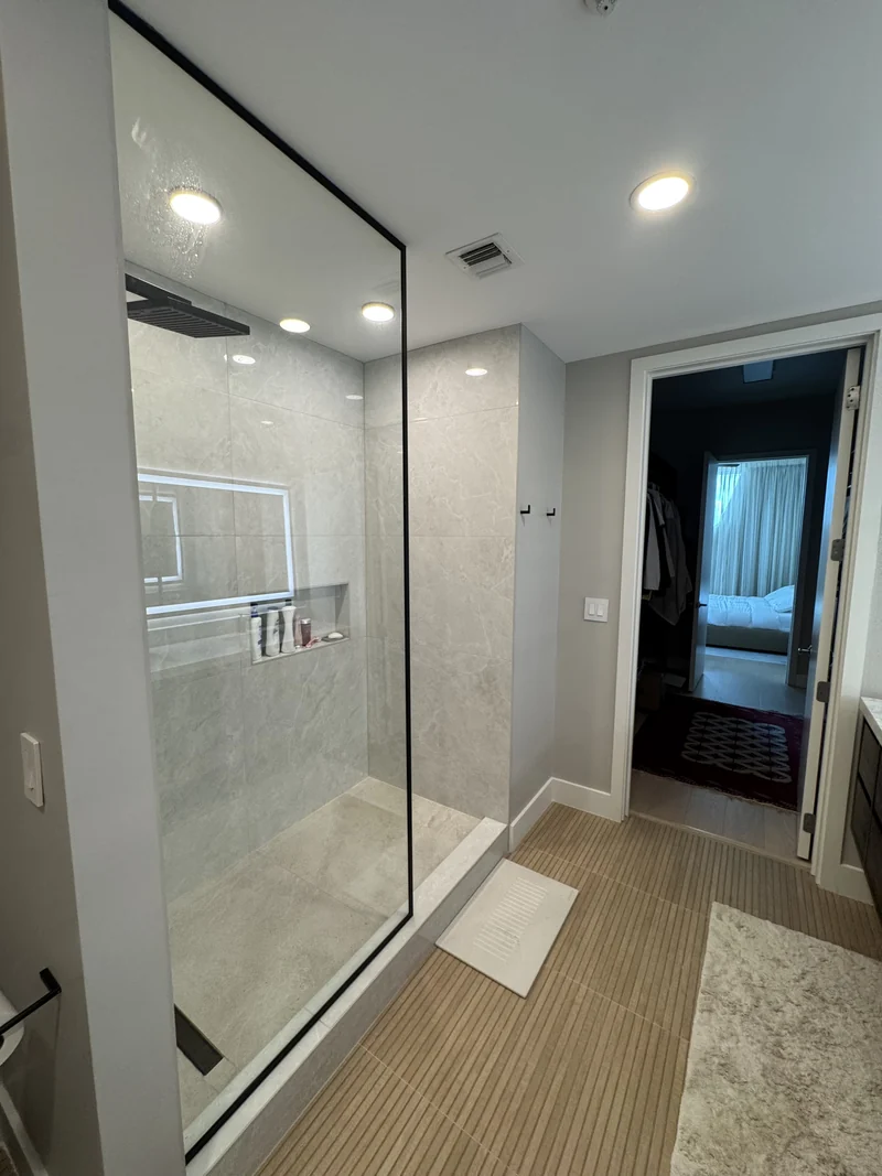 Wood vanity with a pale counter and tall mirror beside a glass shower