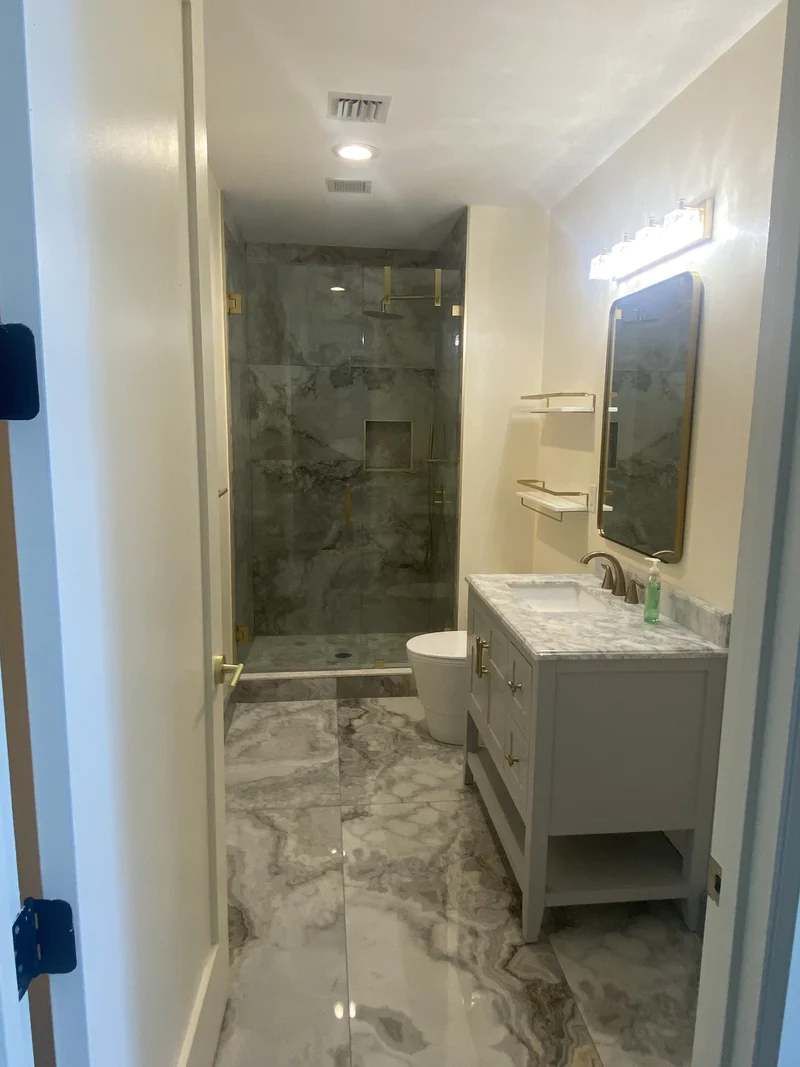 Pale vanity and glass shower with large patterned gray tiles