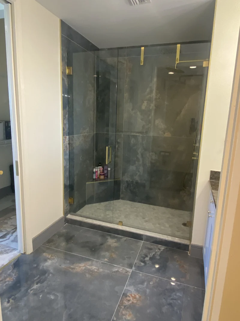 Glass shower with dark veined wall tile and a mosaic floor