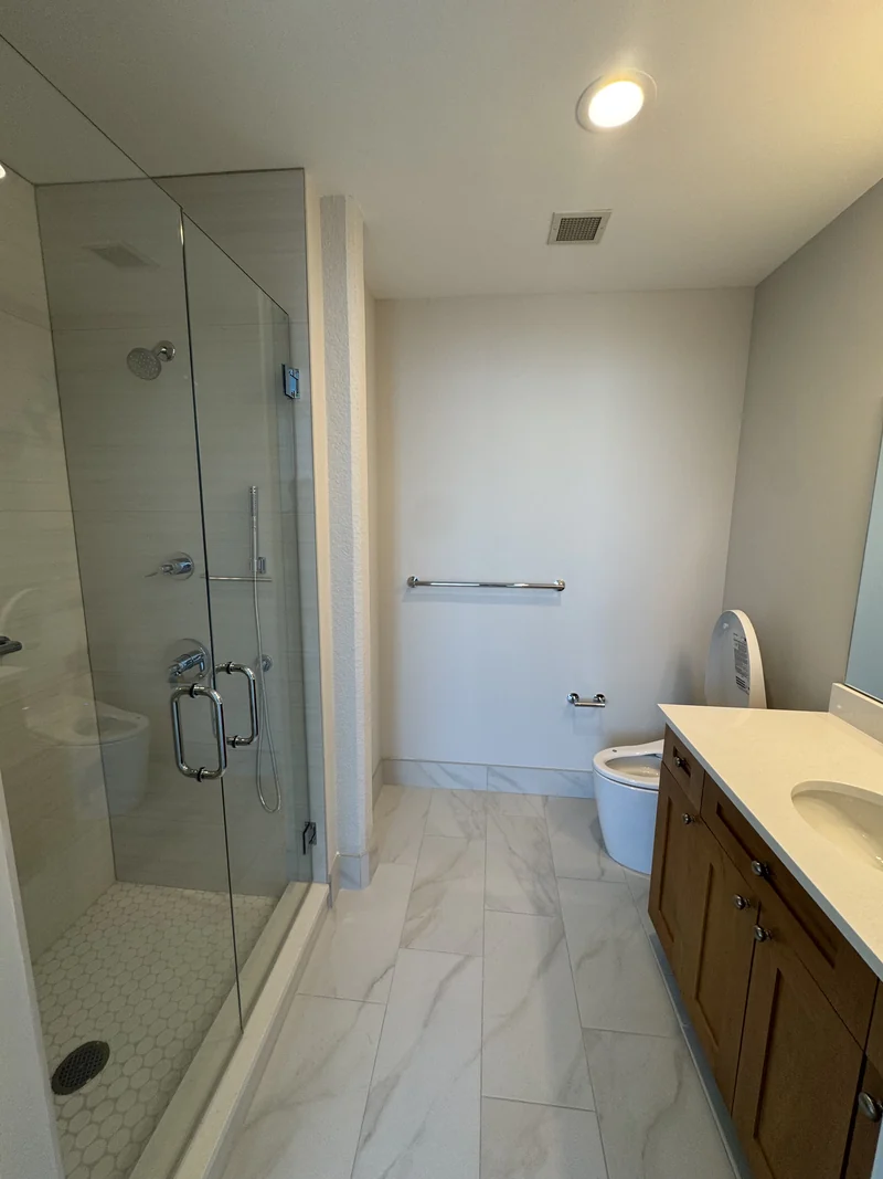 Wood vanity beside a shower with white wall tile and veined floor tile