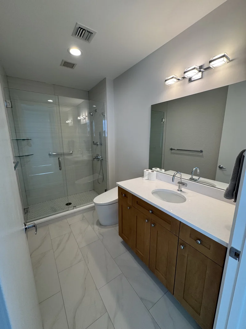 Wood vanity and glass shower with pale wall tile and mosaic flooring
