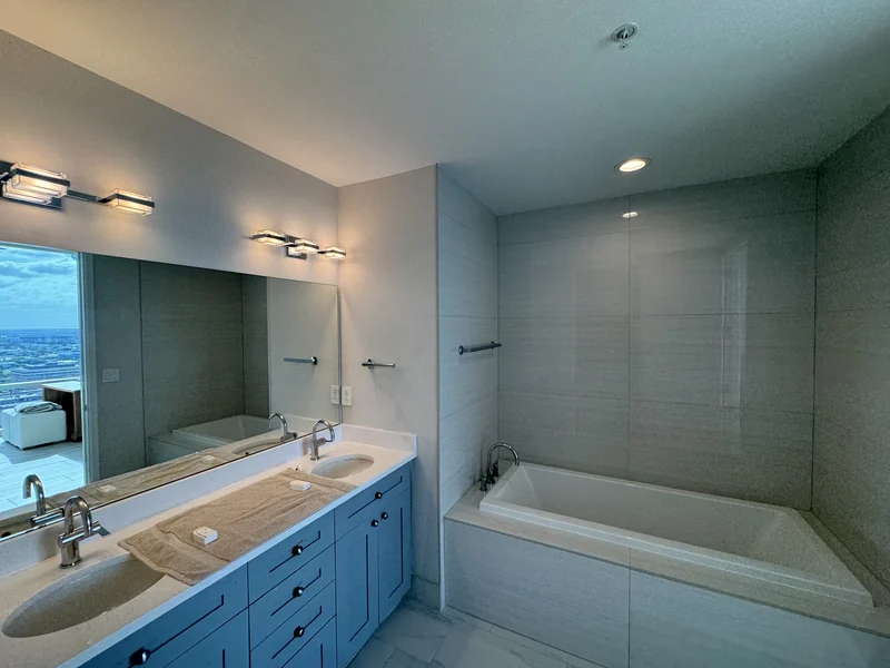 Blue double vanity, glass shower and bathtub with pale wall tile