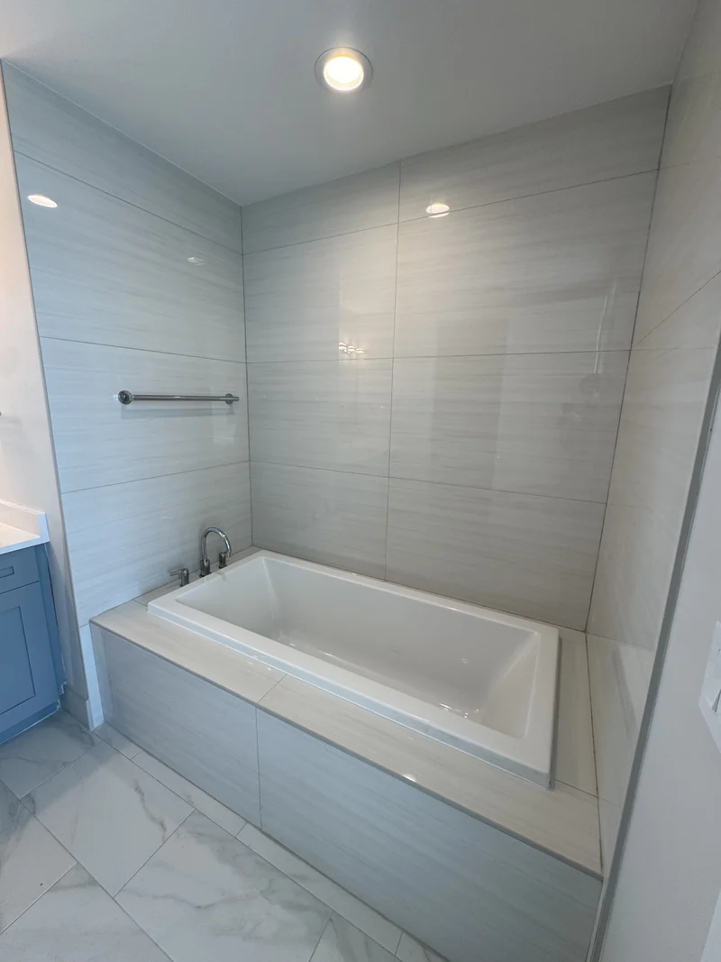 White bathtub with horizontal white wall tile beside a blue vanity