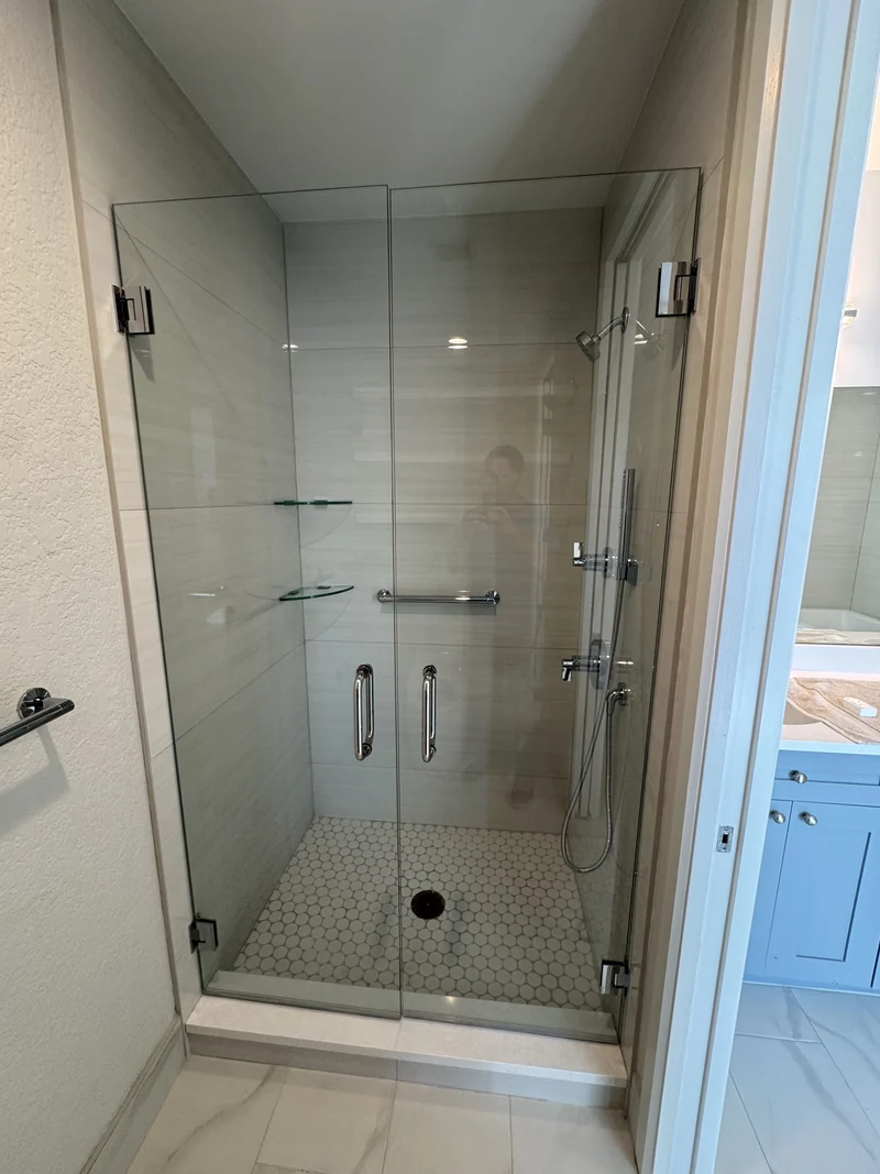 Glass shower enclosure with horizontal white wall tile and round mosaic flooring