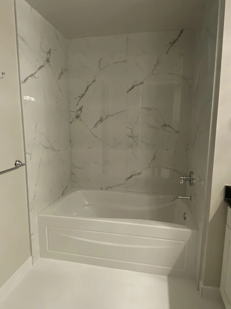 White bathtub enclosed by pale veined wall tile