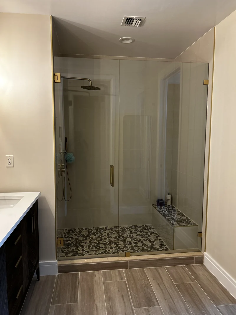 Glass shower enclosure with pale walls, a tiled bench and a pebble-pattern floor