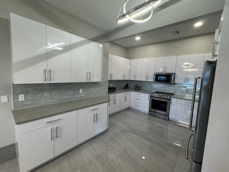 White kitchen cabinets with gray counters, glass tile backsplash and stainless appliances