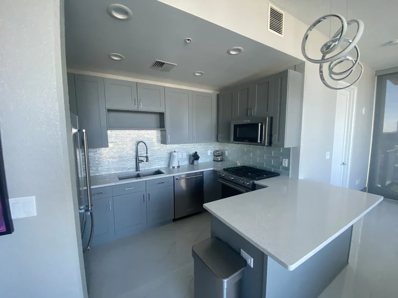 Gray kitchen cabinets and white counters with seating at the peninsula