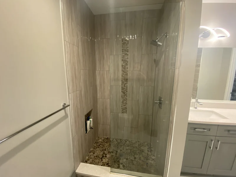 Glass shower enclosure with textured warm-gray tile and a recessed niche
