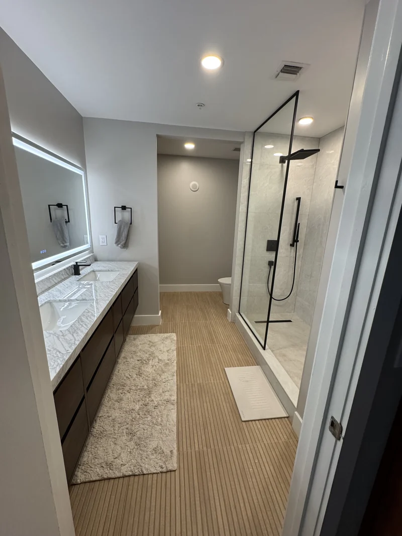 Wood vanity and glass shower enclosure with black hardware and warm floor tile