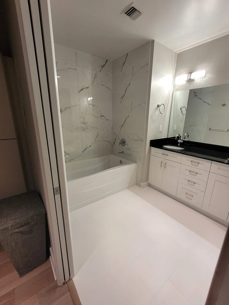 White vanity with dark counter beside a soaking tub and veined wall tile