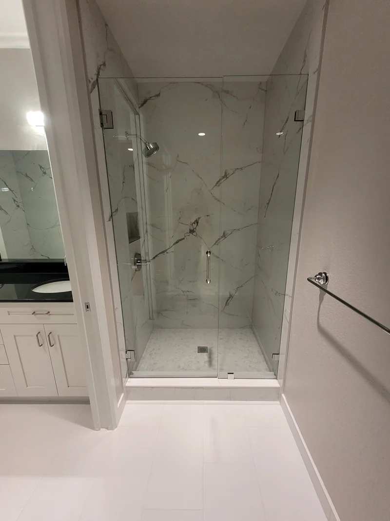 Frameless glass shower with white veined tile and a small square floor mosaic